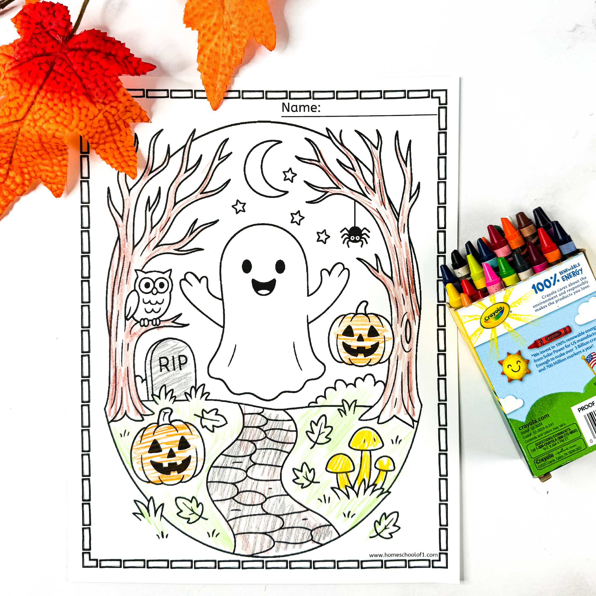 A Halloween ghost coloring page featuring a happy ghost in a spooky forest with pumpkins, tombstones, spider, owl, stars, moon, and mushrooms. A box of crayons lies beside the page, and autumn leaves frame the top of the image.